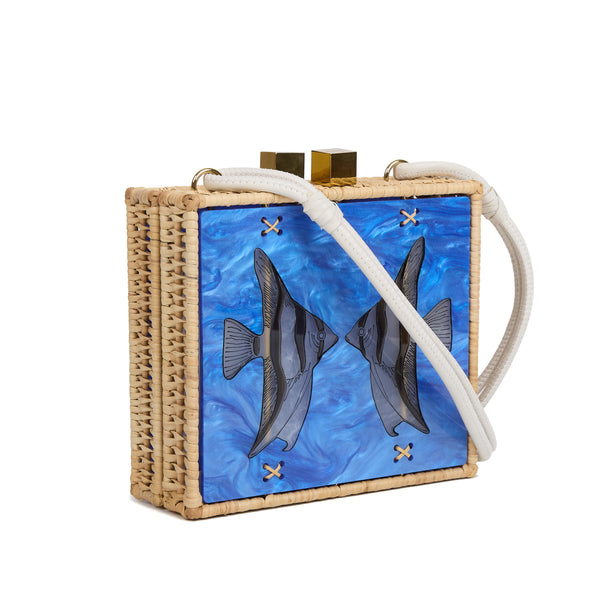 Bolsa quadrada estruturada em rattan com painel em acrílico marmorizado azul, estampa de dois peixes espelhados ao centro, fecho metálico dourado e alça longa em couro branco.