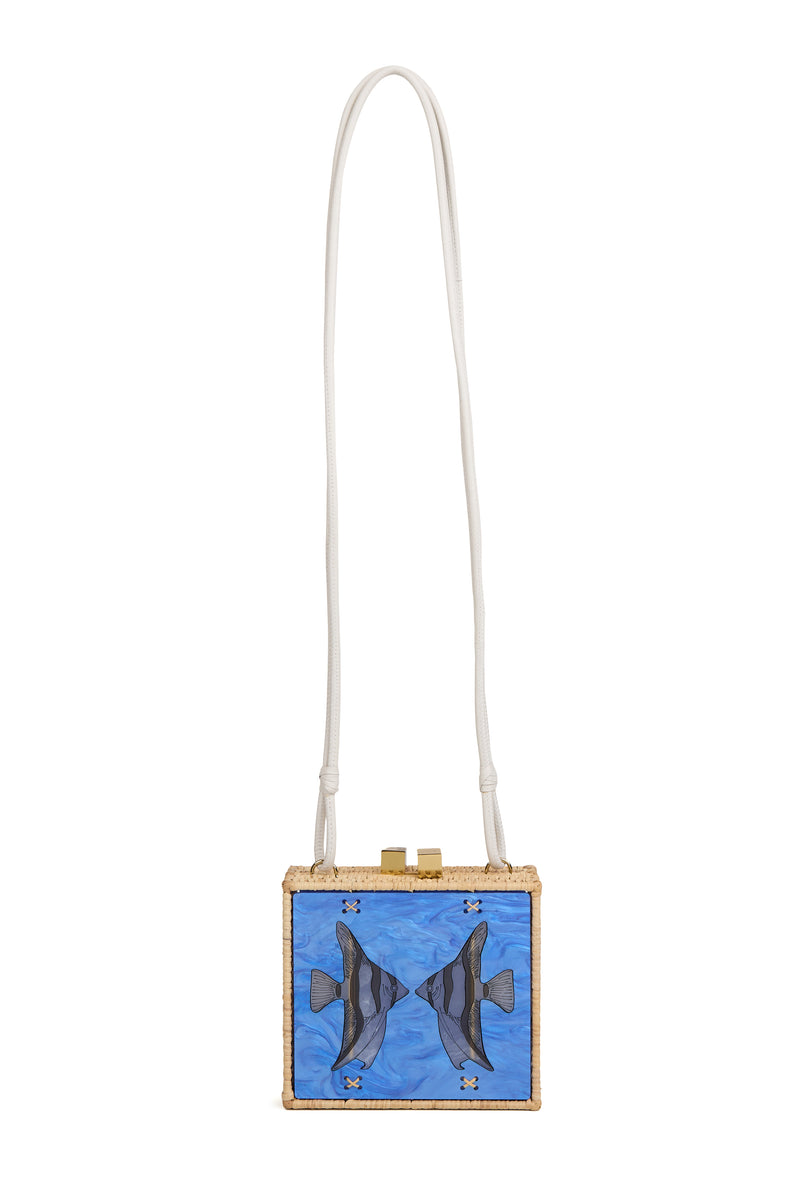 Bolsa quadrada em rattan natural, com estampa central de dois peixes espelhados sobre acrílico marmorizado azul, fecho dourado e alça de couro branco.