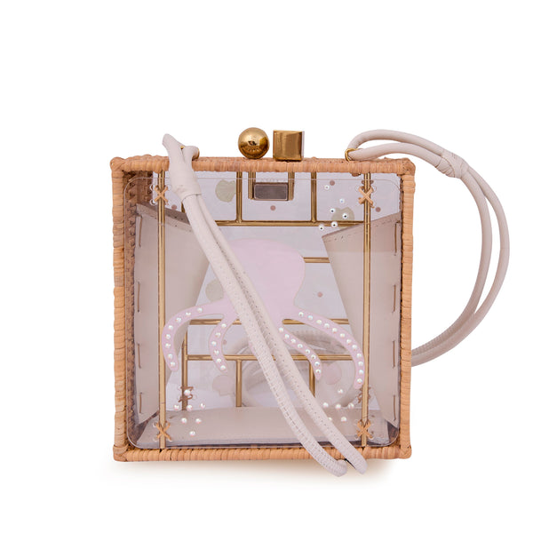 Bolsa quadrada com estrutura em rattan e acrílico transparente, estampa de polvo rosa ao centro com detalhes brilhantes, fecho metálico dourado e alça longa em couro claro.