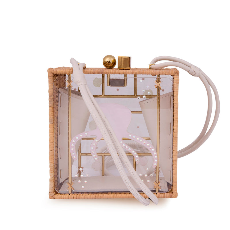Bolsa quadrada com estrutura em rattan e acrílico transparente, estampa de polvo rosa ao centro com detalhes brilhantes, fecho metálico dourado e alça longa em couro claro.