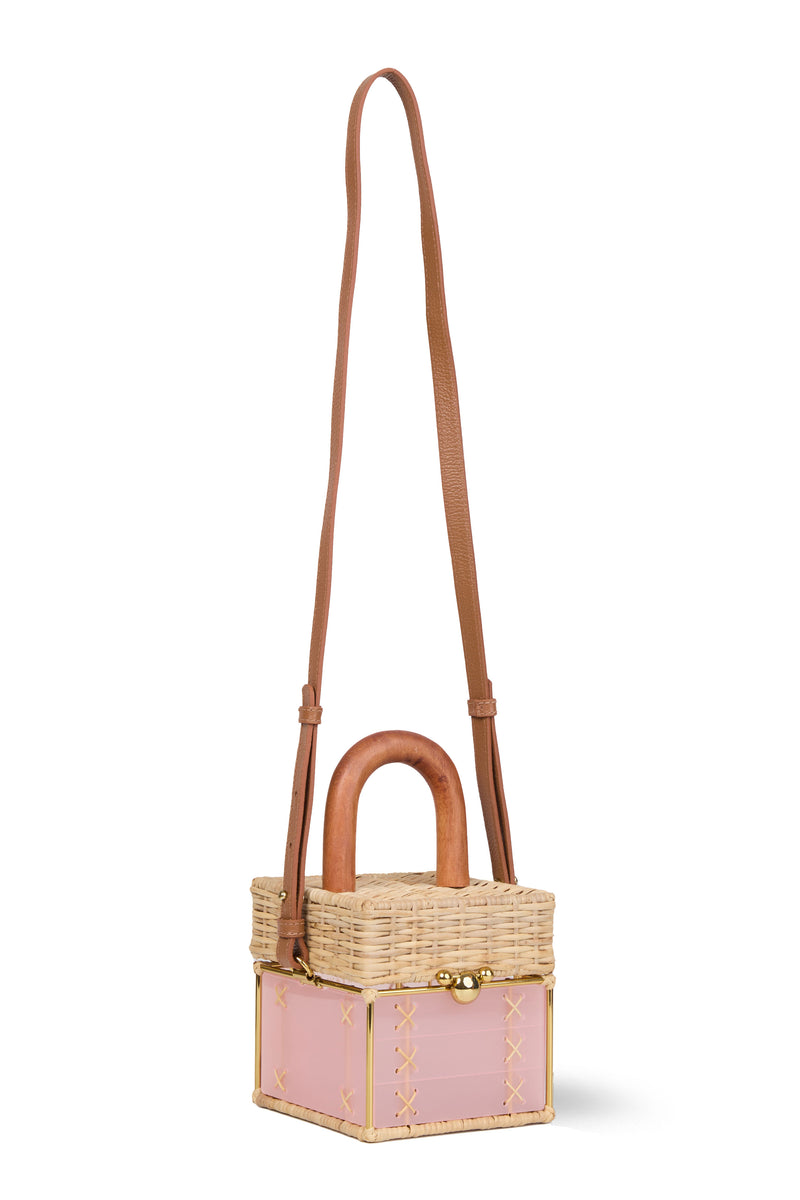 Bolsa pequena estruturada em rattan natural com base em acrílico rosa translúcido, detalhe de costura em X e alça rígida em madeira.