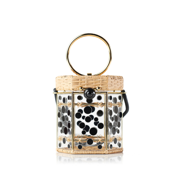 Bolsa estruturada em rattan com corpo em acrílico transparente, aplicações de círculos pretos, fecho esférico preto e alça metálica circular.
