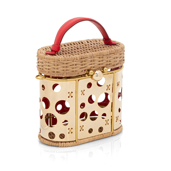 Bolsa em rattan estruturada com painel dourado frontal vazado em círculos, alça curta vermelha em couro e fecho metálico dourado.