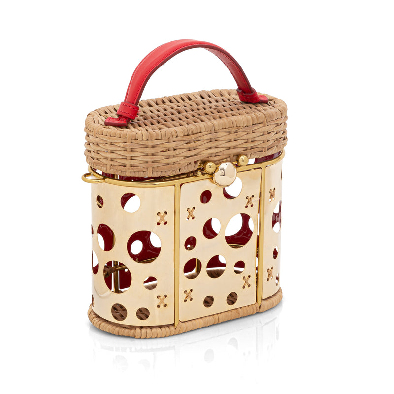 Bolsa em rattan estruturada com painel dourado frontal vazado em círculos, alça curta vermelha em couro e fecho metálico dourado.