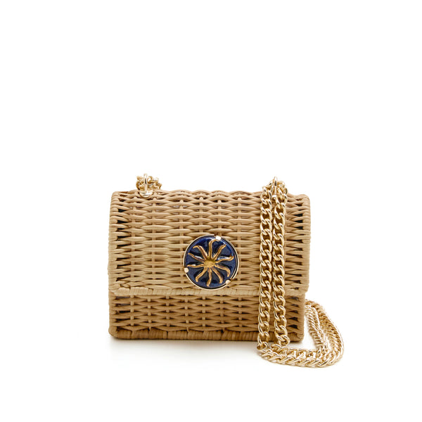 Bolsa estruturada em rattan natural com detalhe central redondo em azul marinho e sol dourado, alça longa de corrente metálica dourada.