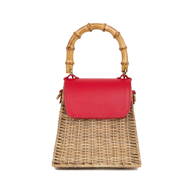 Bolsa estruturada em rattan natural com flap em couro vermelho, detalhe de concha azul central na frente e alça superior em bambu.