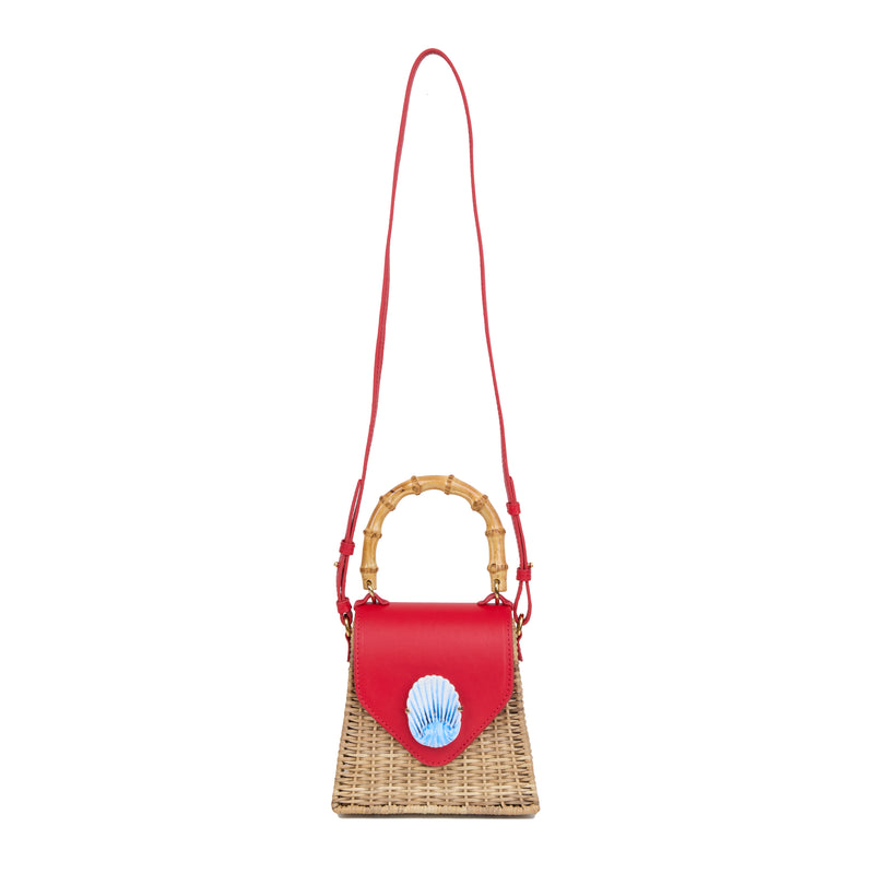 Bolsa estruturada em rattan natural com flap em couro vermelho, detalhe de concha azul central na frente e alça superior em bambu.