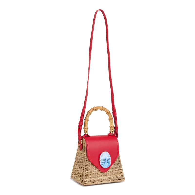 Bolsa estruturada em rattan natural com flap em couro vermelho, detalhe de concha azul central na frente e alça superior em bambu.