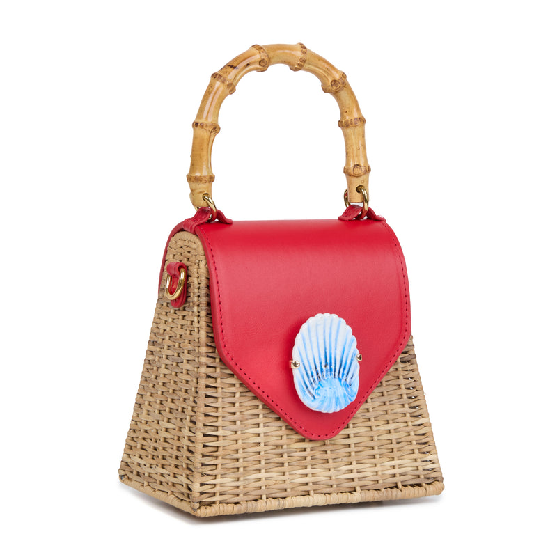 Bolsa estruturada em rattan natural com flap em couro vermelho, detalhe de concha azul central na frente e alça superior em bambu.