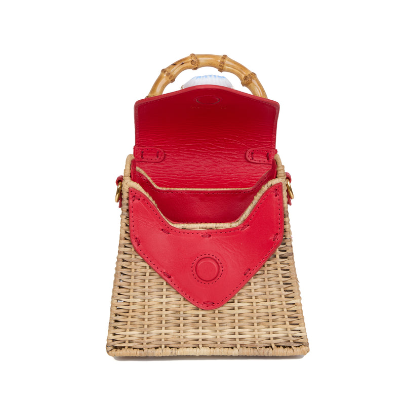 Bolsa estruturada em rattan natural com flap em couro vermelho, detalhe de concha azul central na frente e alça superior em bambu.