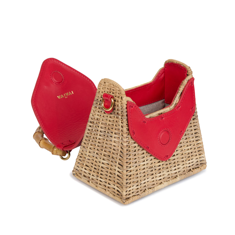Bolsa estruturada em rattan natural com flap em couro vermelho, detalhe de concha azul central na frente e alça superior em bambu.