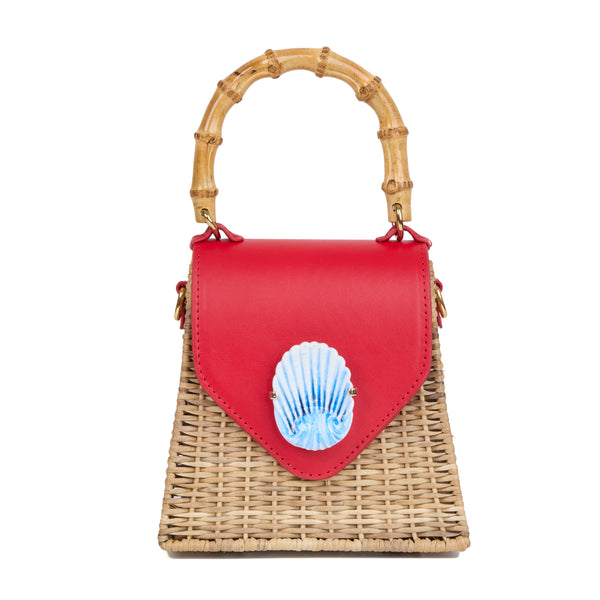 Bolsa estruturada em rattan natural com flap em couro vermelho, detalhe de concha azul central na frente e alça superior em bambu.