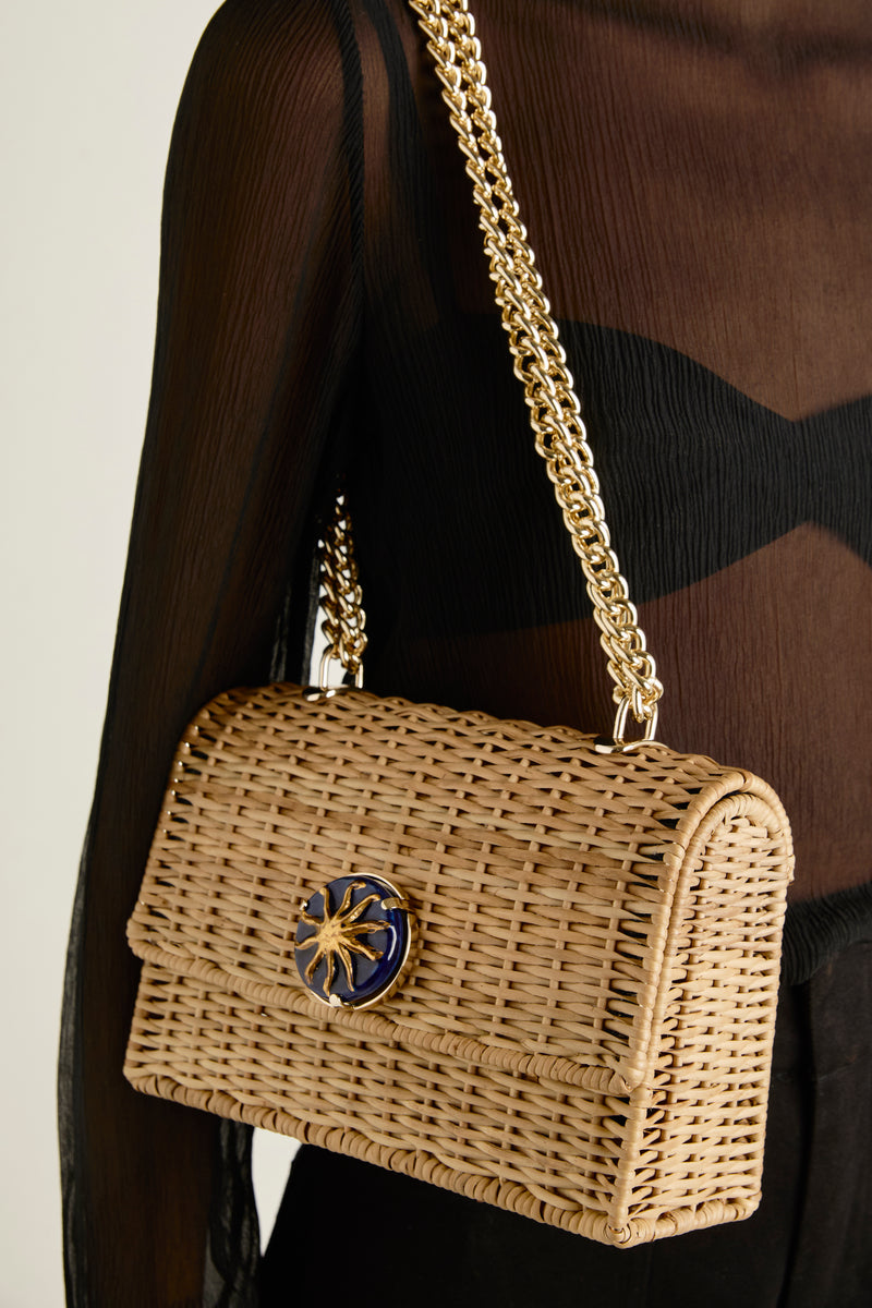 Bolsa estruturada de rattan natural em tamanho maior, com aplique redondo azul marinho e sol dourado, finalizada com corrente dourada.