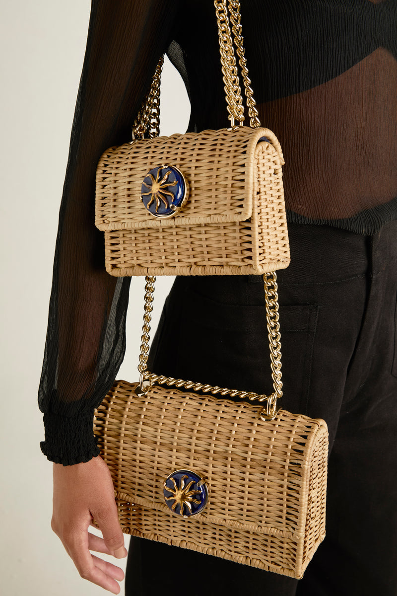 Bolsa autoral estruturada em rattan natural grande, com detalhe circular azul marinho e sol dourado, alça de corrente dourada.