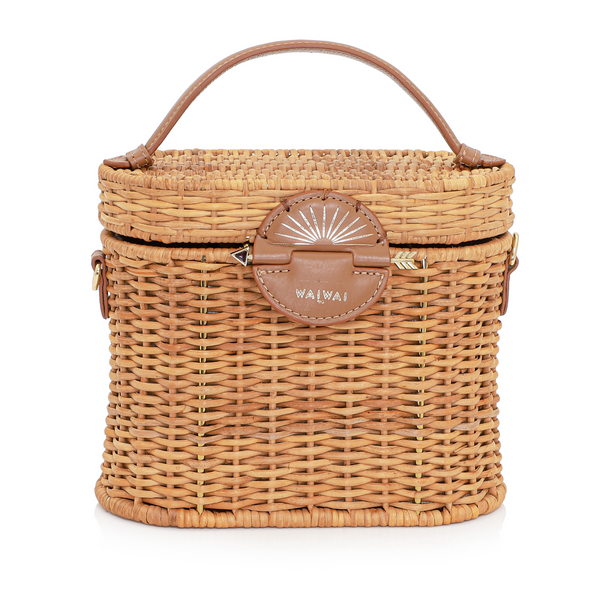 Bolsa de rattan natural com alça curta em couro bege e fecho circular em couro com detalhe em formato de raio de sol dourado.