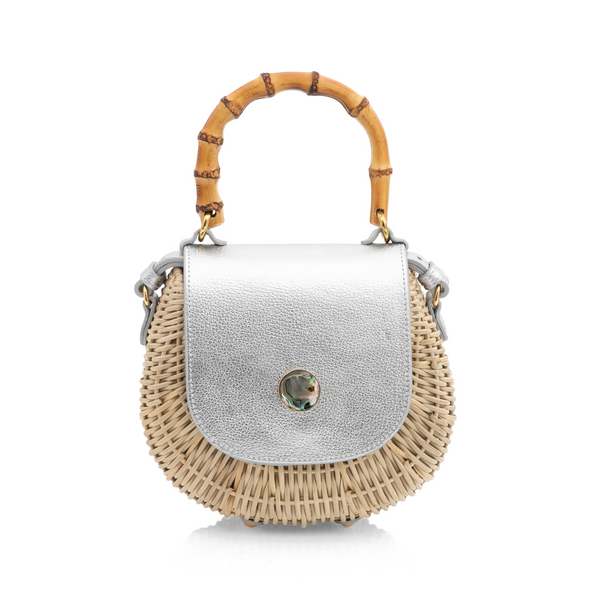 Bolsa estruturada em rattan natural com tampa em couro prateado metalizado, detalhe de fecho circular em madrepérola e alça superior em bambu curvado.