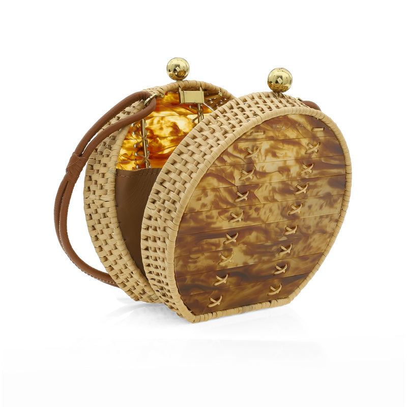 Bolsa redonda em acrílico marmorizado caramelo, com alça longa em couro marrom, detalhes em palha trançada nas bordas e fecho esférico dourado.