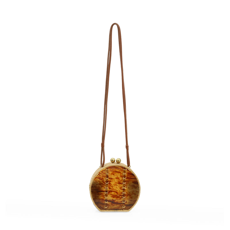 Bolsa redonda em acrílico marmorizado caramelo, com alça longa em couro marrom, detalhes em palha trançada nas bordas e fecho esférico dourado.