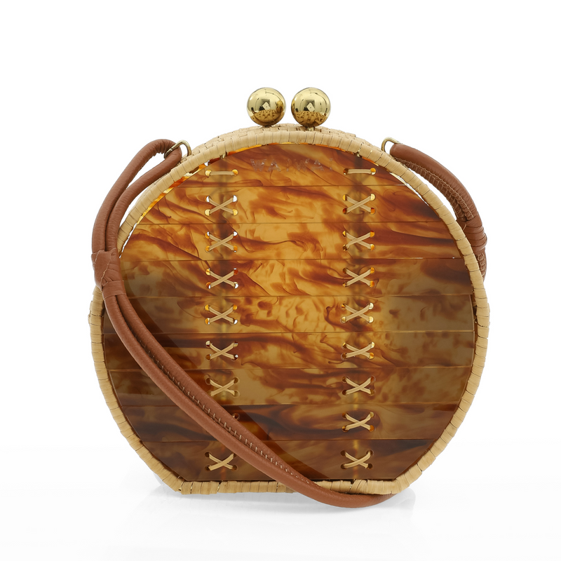Bolsa redonda em acrílico marmorizado caramelo, com alça longa em couro marrom, detalhes em palha trançada nas bordas e fecho esférico dourado.