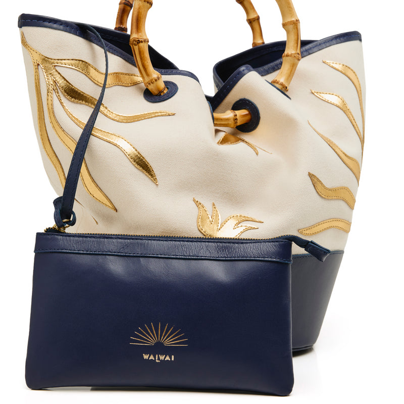 Bolsa tote em tecido cru com bordados dourados, base em azul marinho e alça estruturada em bambu.