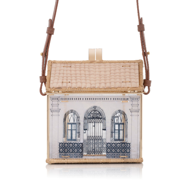 Bolsa estruturada em formato de casa, feita em acrílico branco e vime trançado, com janelas e portas azuis inspiradas no bairro do Carmo.