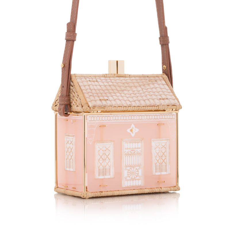 Bolsa estruturada em formato de casa, feita em acrílico nude e vime trançado, com tampa em formato de telhado e estrutura dourada.
