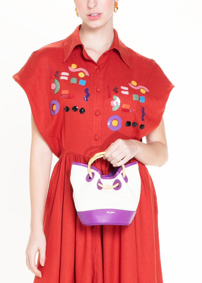 Bolsa bucket artesanal em canvas cru, alça de mão em bambu curvado e acabamento em couro roxo na base e nas bordas.