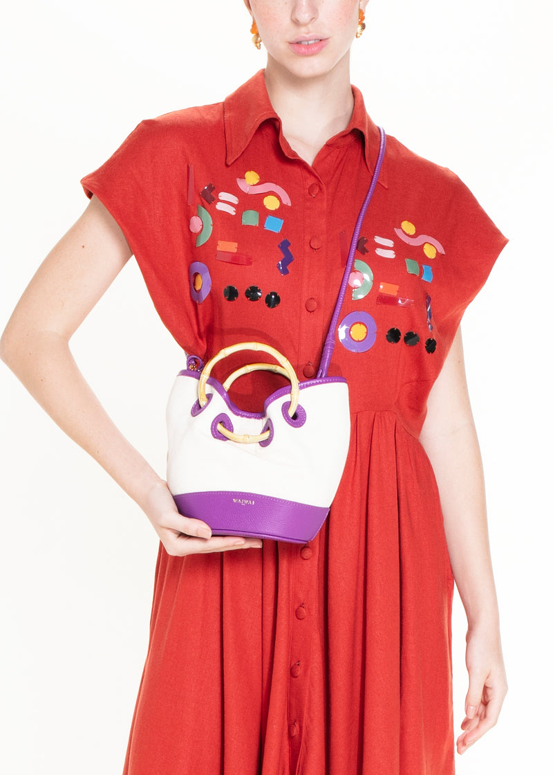 Bolsa bucket de canvas cru estruturada, com detalhes em couro roxo, alça de bambu curvado e reforços em couro.
