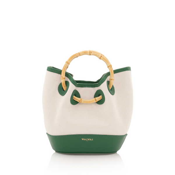 Bolsa bucket em canvas bege com acabamento em couro verde e alça de bambu natural. Elegância tropical e atemporal.