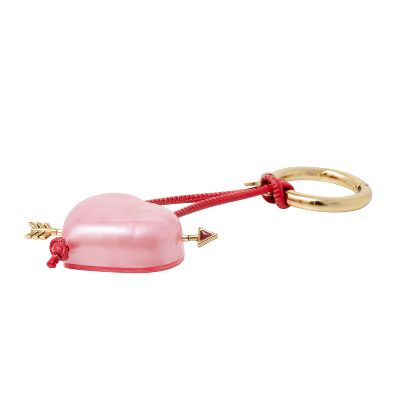 Acessório artesanal em acrílico rosa, com formato de coração e detalhe de flecha dourada.