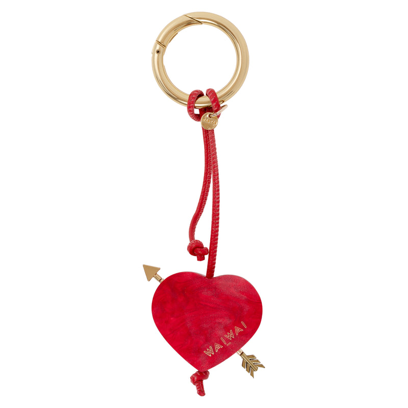 Pingente em formato de coração vermelho com flecha dourada e argola metálica dourada.