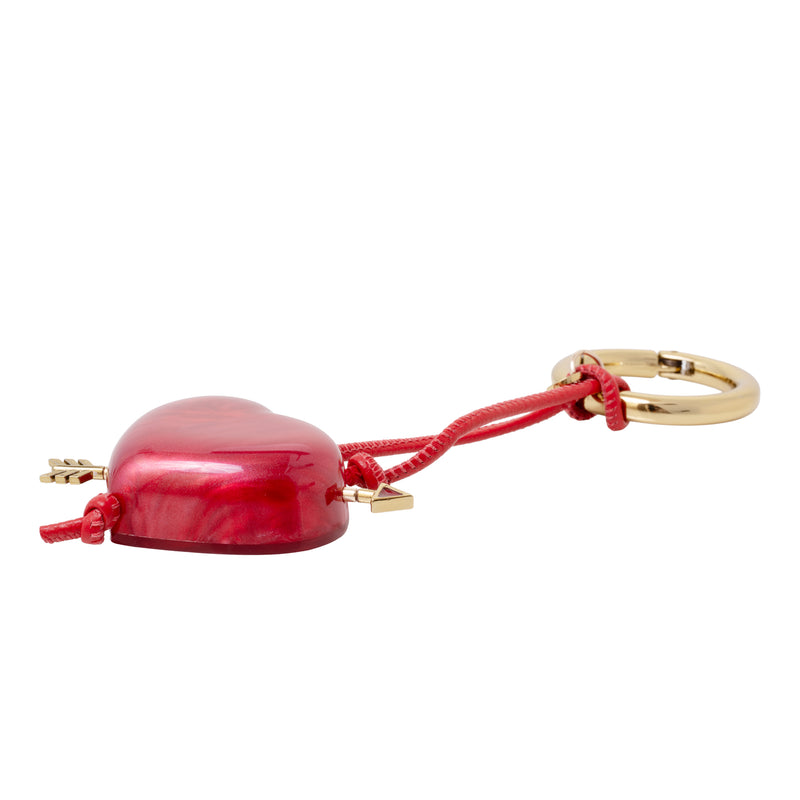 Acessório artesanal em acrílico vermelho, com formato de coração e detalhe de flecha dourada.