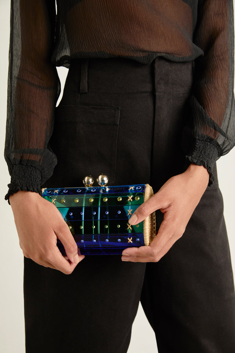 Clutch em acrílico azul e verde translúcido com design geométrico, acabamentos em palha nas laterais e fecho dourado no topo.