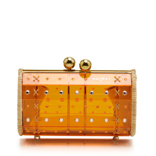 Clutch em acrílico laranja translúcido com aplicações geométricas, detalhes em palha nas laterais e fecho esférico dourado.