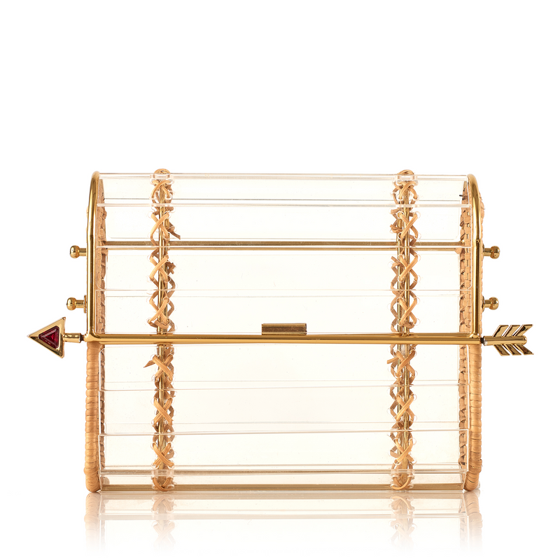 Clutch em acrílico transparente com laterais em rattan, detalhe de costura em X dourado e fecho em formato de flecha metálica dourada com ponta vermelha.