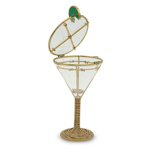Taça transparente em acrílico com estrutura metálica dourada, haste e base em rattan trançado e aplicação de limão verde na borda.
