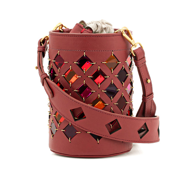 Bolsa bucket estruturada em couro vinho, com recortes em losangos que exibem detalhes coloridos em efeito espelhado. Alça longa ajustável e fechamento por cordão interno.