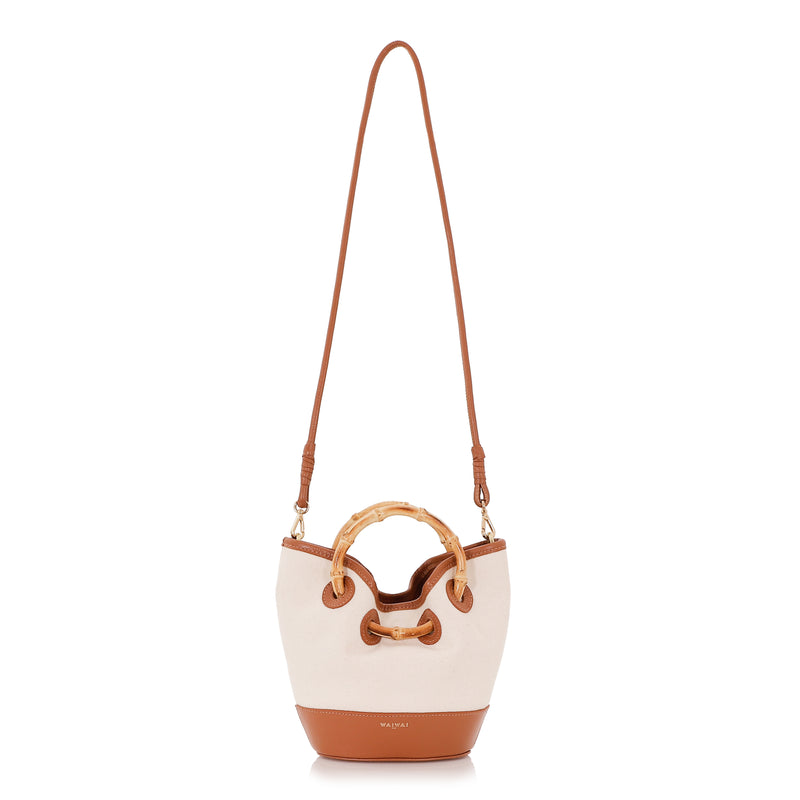 Bolsa bucket em linho cru com base e detalhes em couro caramelo, alça estruturada em bambu natural e fechamento por amarração.