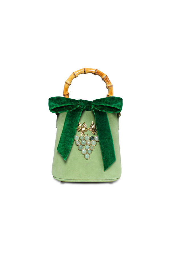 Bolsa bucket em camurça verde com alça de bambu e detalhe frontal de cacho de uvas formado por pedras verdes e folhas metálicas douradas.