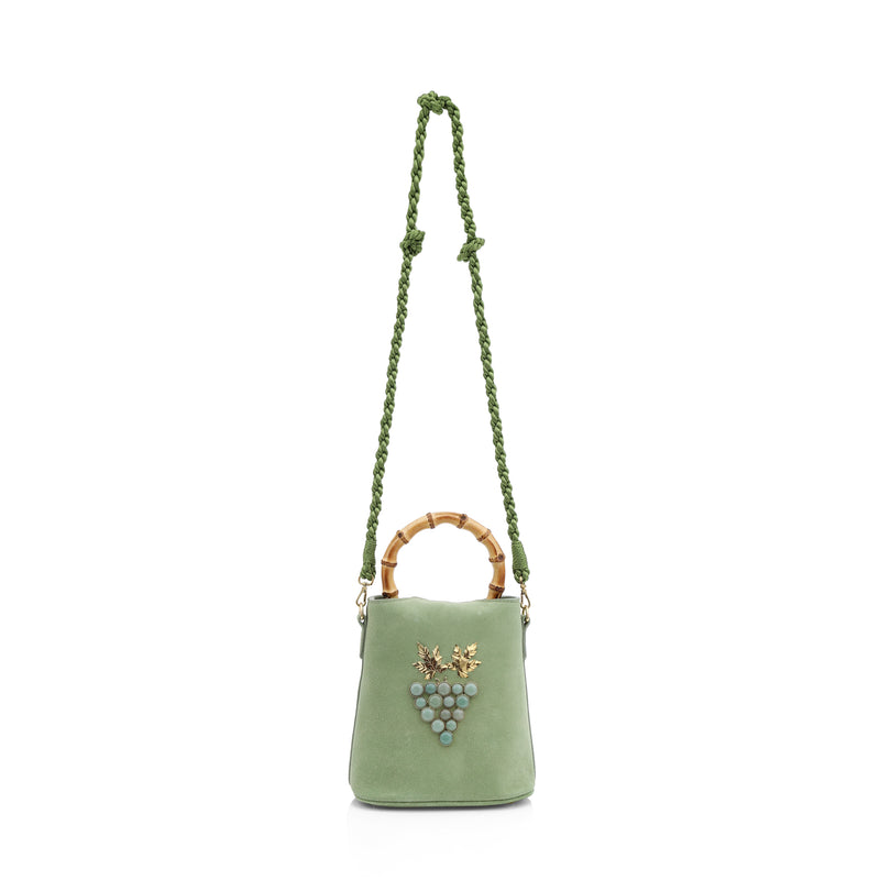 Bolsa bucket estruturada em camurça verde com alça em bambu e ornamento frontal de cacho de uvas em pedras verdes e folhas metálicas douradas.