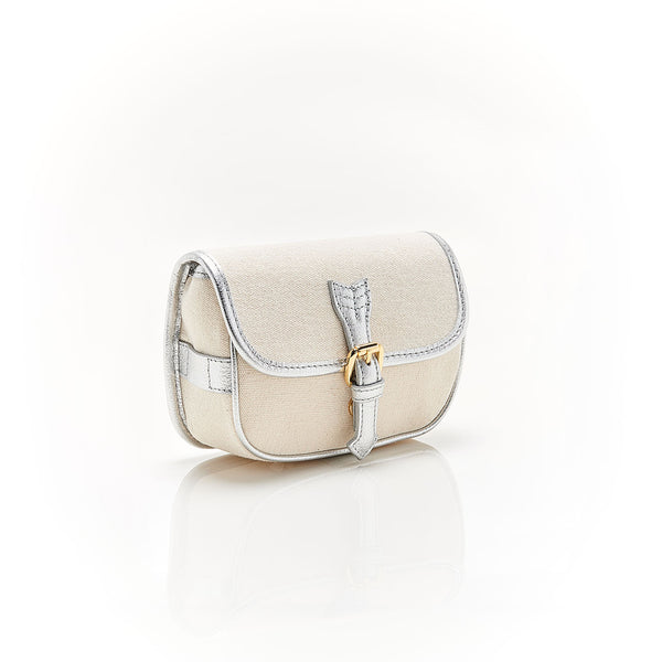 Bolsa em canvas cru com detalhes em couro prateado metálico e fivela dourada, podendo ser usada como crossbody ou pochete.