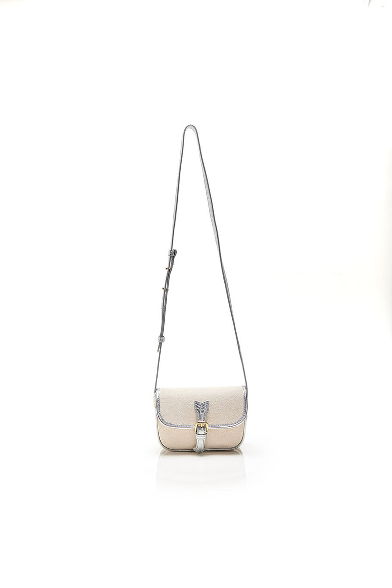 Bolsa de canvas cru com detalhes em couro metálico prata e fivela dourada, podendo ser ajustada na cintura como pochete ou usada a tiracolo.