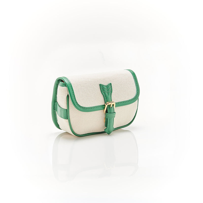 Bolsa de canvas cru com acabamento em couro verde e fivela dourada, versátil para ser usada tanto como crossbody com alça longa quanto como pochete ajustada na cintura.