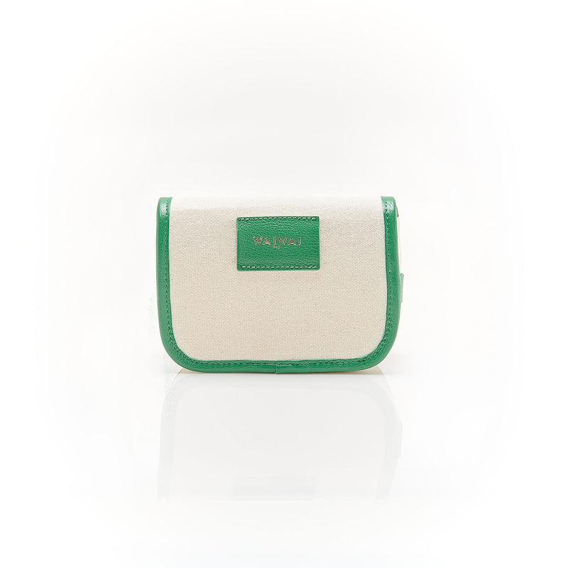 Bolsa de canvas cru com acabamento em couro verde e fivela dourada, versátil para ser usada tanto como crossbody com alça longa quanto como pochete ajustada na cintura.