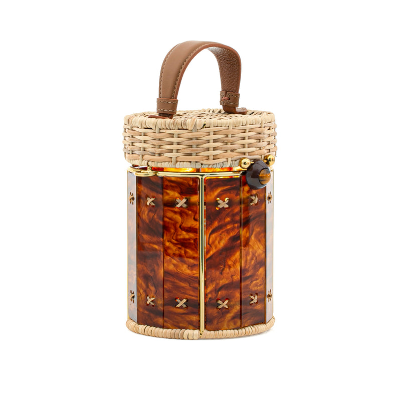 Bolsa estruturada cilíndrica em rattan e acrílico marmorizado âmbar, finalizada com fecho metálico dourado e alça curta em couro marrom.