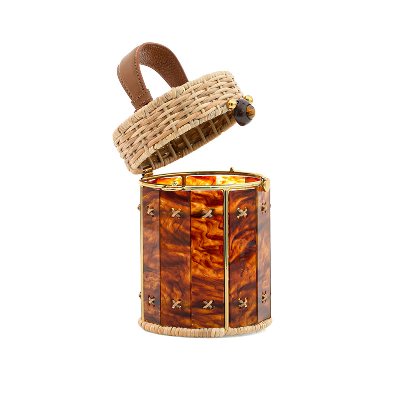 Bolsa em formato cilíndrico, feita em rattan e acrílico âmbar marmorizado, com fecho dourado e alça curta em couro marrom.