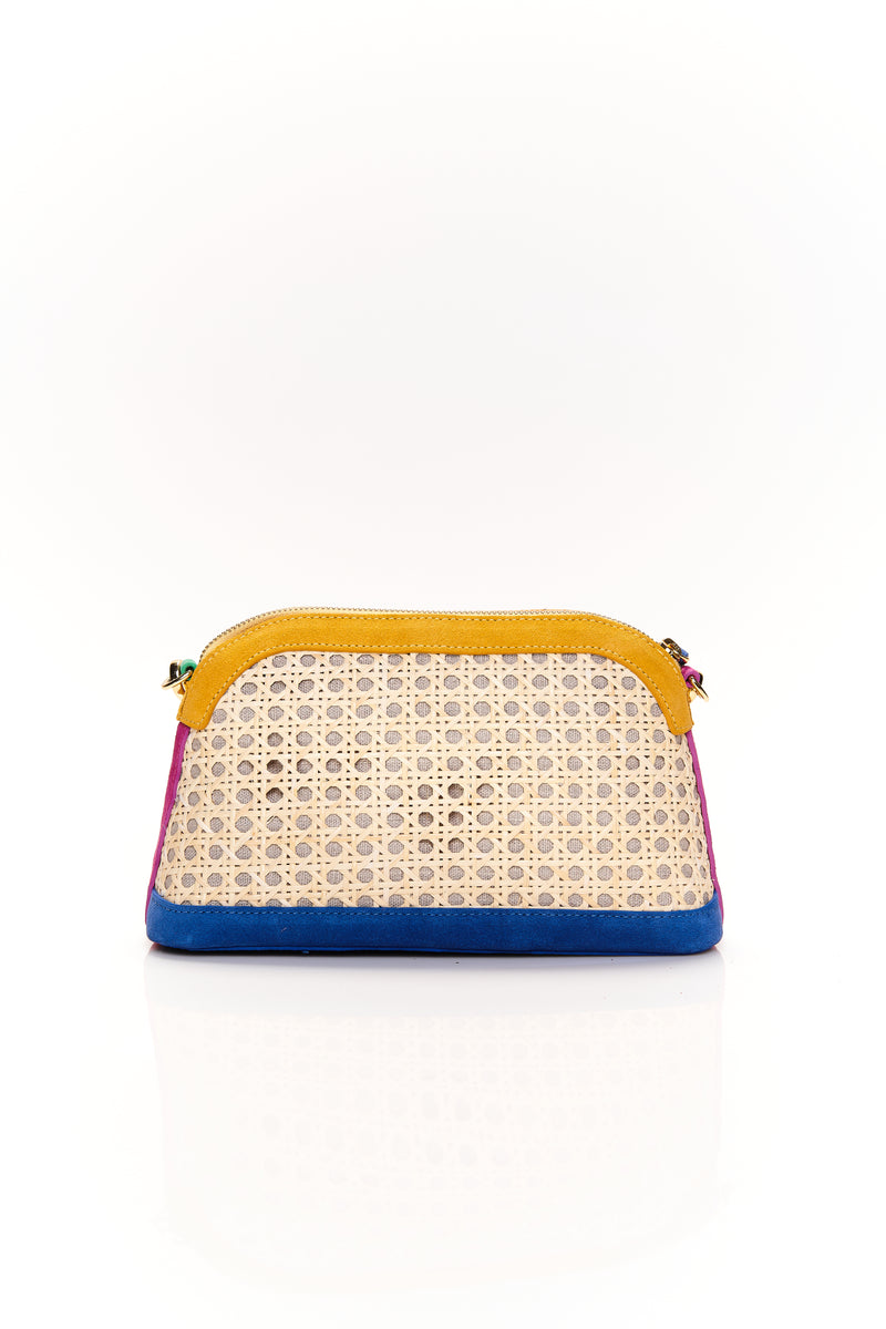 Bolsa estruturada com corpo em palha tramada natural, acabamentos em camurça colorida — amarelo, azul e pink — e alça tiracolo regulável em couro vermelho. Detalhe de plaquinha verde com logo na frente.