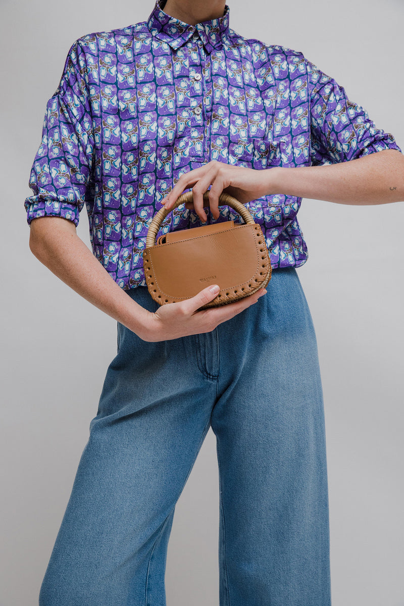 Bolsa de couro marrom claro com detalhe de costura trançada nas laterais e alça estruturada revestida em vime natural.