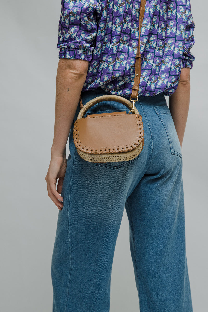 Bolsa de couro marrom claro com detalhe de costura trançada nas laterais e alça estruturada revestida em vime natural.