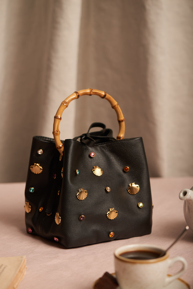 Bolsa em couro preto com aplicações de conchas douradas e cristais coloridos, alça rígida em bambu.